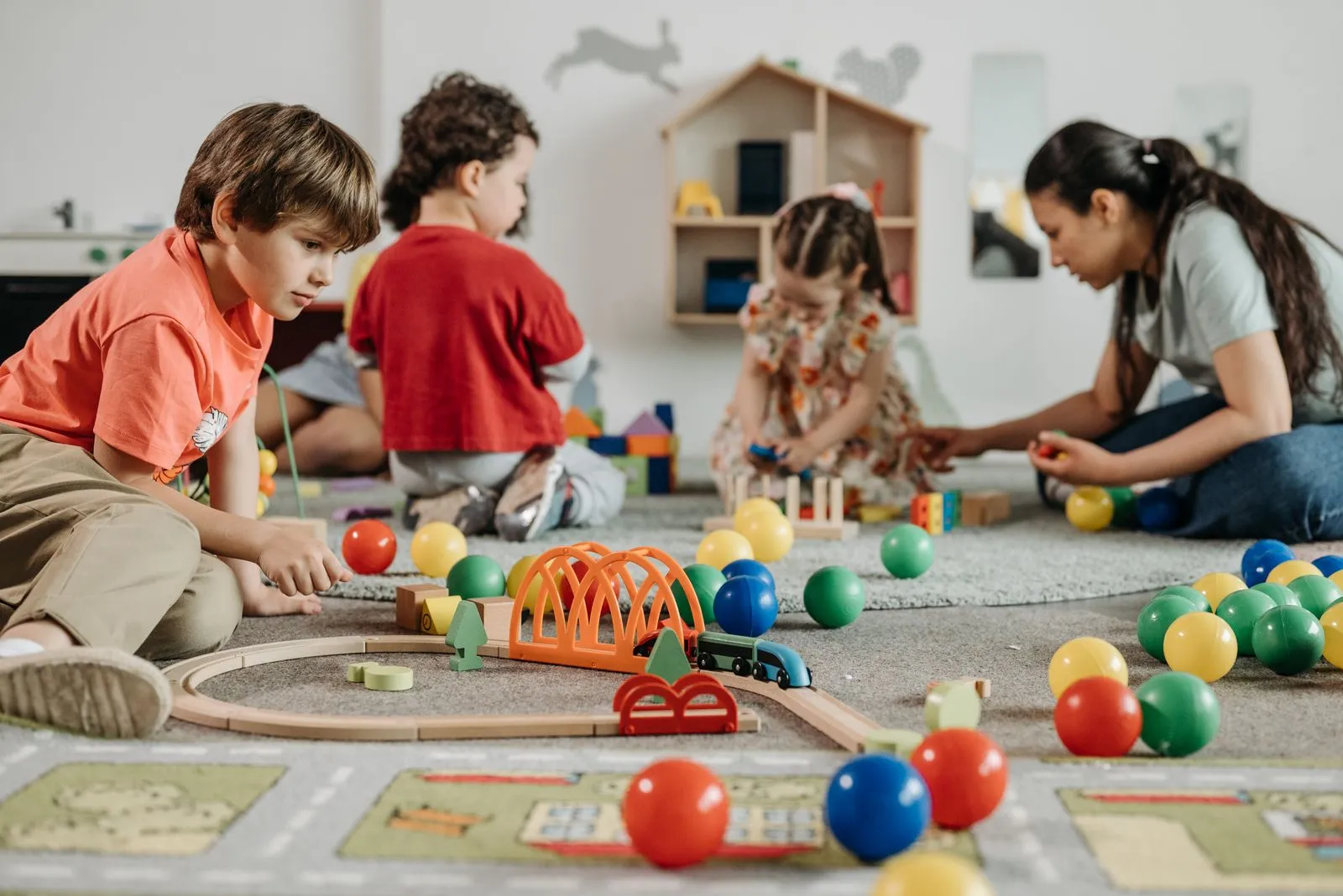 Educadora brincando com crianças no chão de uma sala colorida
