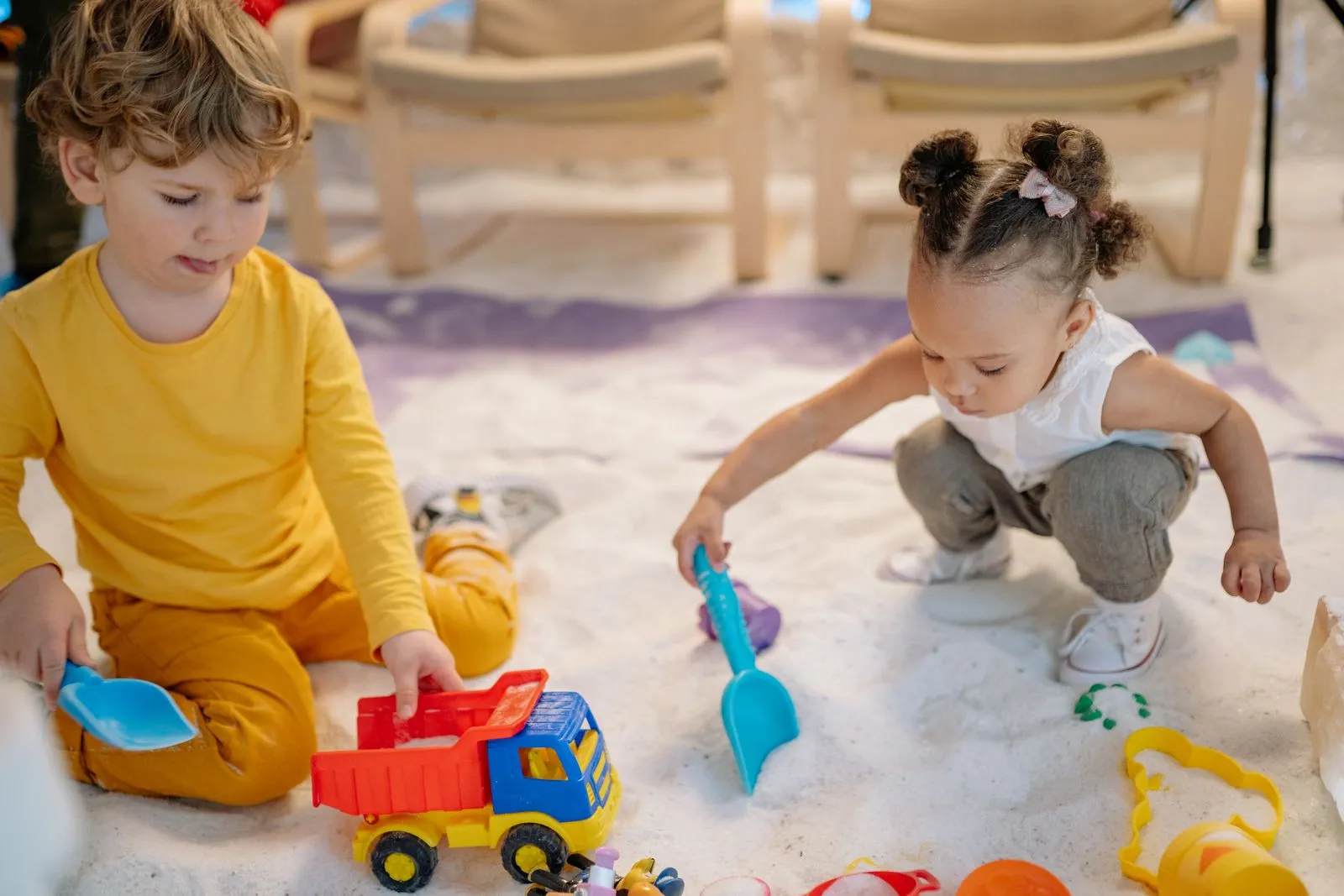 Duas crianças brincando na areia com brinquedos